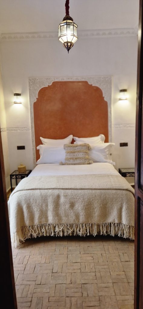Suite Terre du Riad Babmoon : tête de lit en arc terre cuite, lanterne marocaine et sol en briques